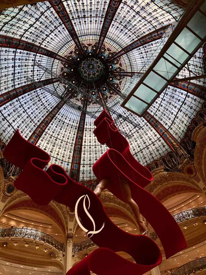 Stained-glass window dome at the Galeries Lafayette in Paris. A red ribbon-like metal sculpture is in the foreground.