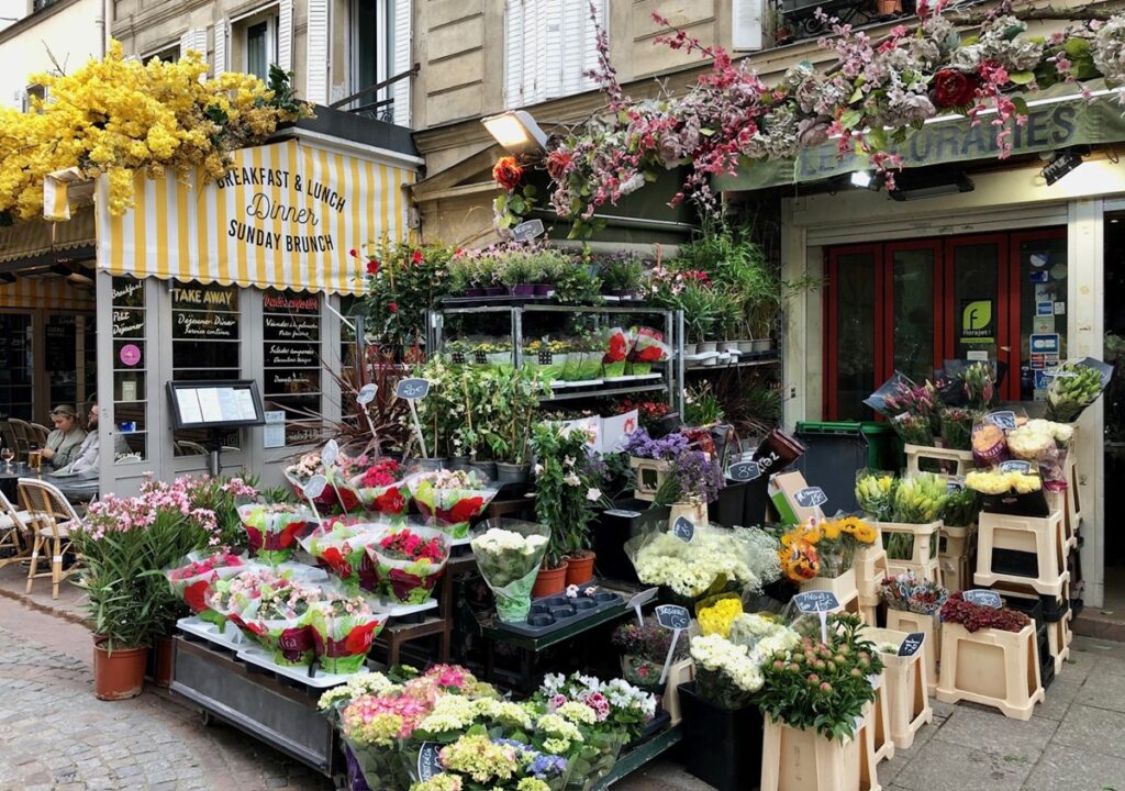 Flower shop with colorful bouquets in Rue Cler. A cafe in the background with a yellow awning.